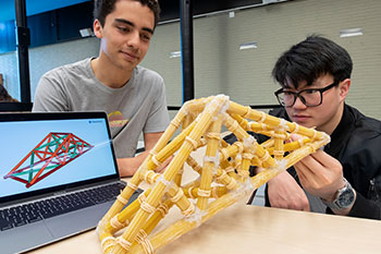 Two male students engineering a model bridge