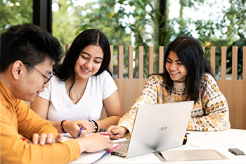 Three students gathered around laptop studying