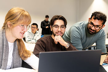 Three students in classroom on laptop studying