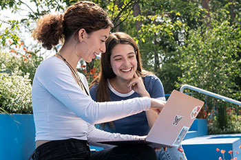 Two female students studying on laptop and campus outside