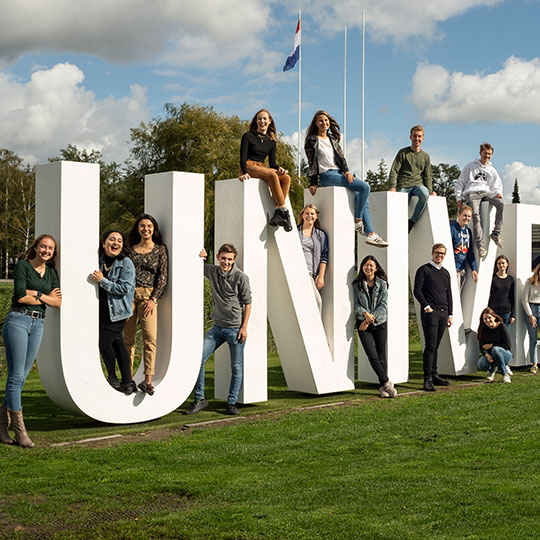 Students sitting on giant white letters spelling university